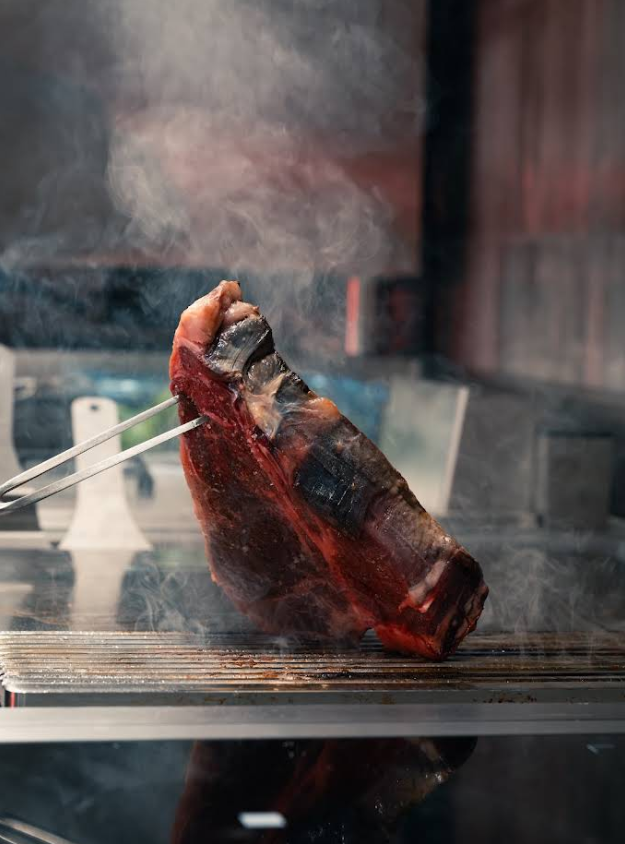 Un gros morceau de bœuf cru sur un gril, fumant.