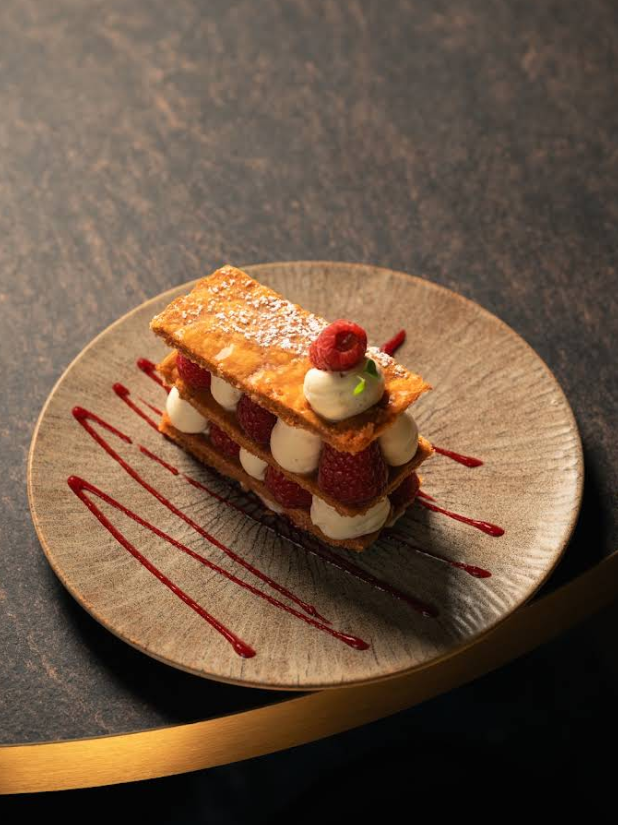 Mille-feuille aux framboises et crème pâtissière, décoré de sucre glace et de coulis.