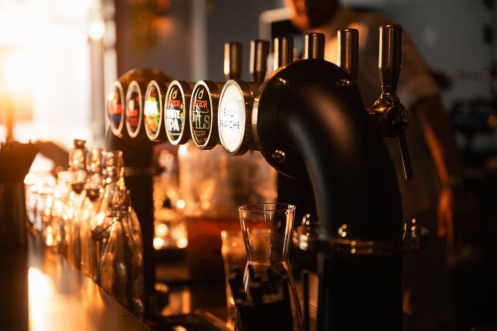 Tireuse à bière avec verres et bouteilles dans un bar éclairé par le soleil.