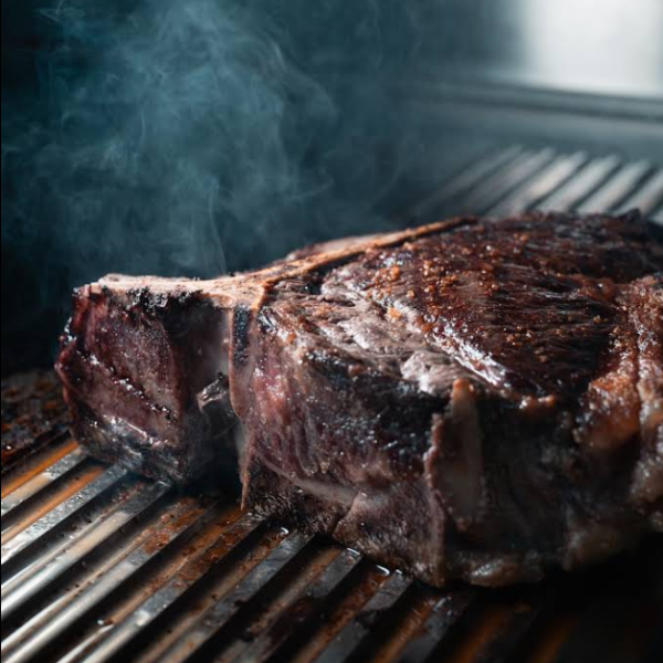 Un gros steak de bœuf juteux grésille sur un grill chaud avec de la vapeur.