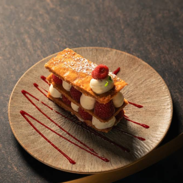 Mille-feuille aux framboises et crème pâtissière, décoré de sucre glace et de coulis.